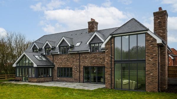 large detached house with conservatory on one side and curtain walling glass facace on the other on a sunny day with lawn